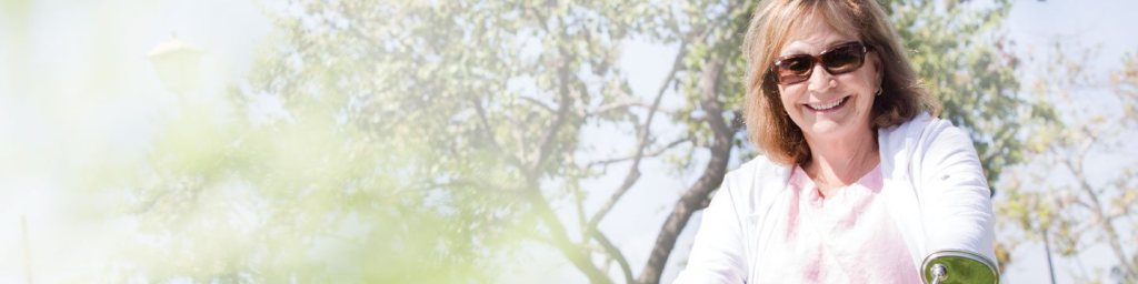Mujer mayor sonriente con gafas de sol y blusa rosa al aire libre